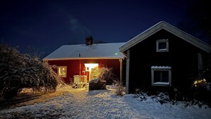 Una casa roja con tejado nevado y un porche iluminado.