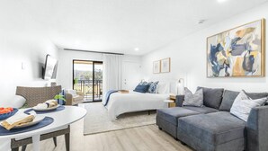 A modern, well-lit hotel room with a bed, grey sofa, and a dining area with a table and chairs. - Golf Course Views | Upscale Studio | Wesley Chapel | Sleeps 2, Pickleball Included | Saddlebrook (Zephyrhills)
