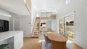 A modern kitchen with a white countertop, wooden staircase, and a dining area with a wooden table and chairs. - The White Nest by Ready Set Stay (San Remo)