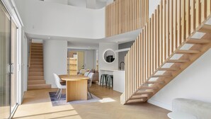 A modern interior with a wooden staircase, a dining area with a round table, and a kitchen with stools. - The White Nest by Ready Set Stay (San Remo)