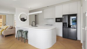 A modern kitchen with white cabinetry, a central island with stools, a built-in oven, and a refrigerator. - The White Nest by Ready Set Stay (San Remo)