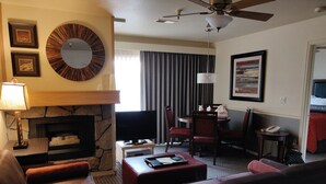 A hotel room with a fireplace, a sofa, a TV, a dining area with chairs, and a ceiling fan. - 2 bd suite/6p in Cozy Boutique Lodge between the slopes and Lake Tahoe near all (South Lake Tahoe)