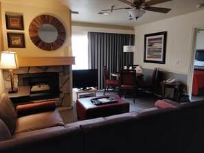Habitación de hotel con chimenea, un sofá, televisor, zona de comedor con sillas y ventilador de techo.