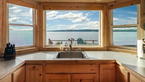 Eine Küche mit einem großen Fenster mit Blick auf einen See, Holzschränken und einer Spüle aus Edelstahl.