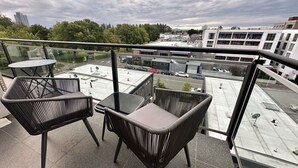 Un balcone con due poltrone in vimini e un tavolino, con vista su un'area di parcheggio e degli edifici.