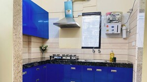 A kitchen with blue cabinets, a gas stove, a stainless steel range hood, and a window with a view. - Jolo Hotel Gurgaon and Birthday Venues (Gurugram)