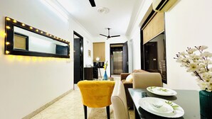 A modern living room with a sofa, a yellow chair, a dining table with plates and a vase of flowers. - Jolo Hotel Gurgaon and Birthday Venues (Gurugram)