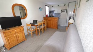 Een woonkamer met een televisie, houten meubels, een bank en een keukenhoek met een magnetron.