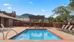 Una piscina con sillas de descanso y una pérgola de madera, rodeada por una valla de madera y una montaña al fondo.