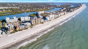 Ett hotell vid kusten med flera byggnader längs stranden, en småbåtshamn och en flod i bakgrunden.