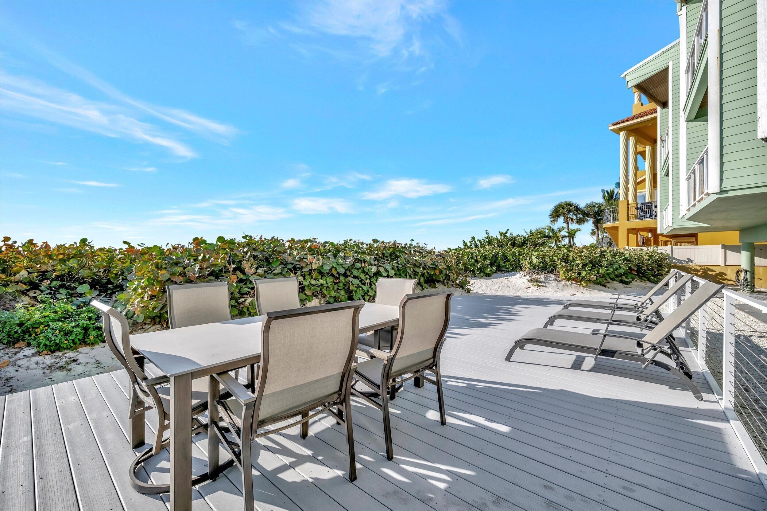 A deck with a table and chairs, a pool area with lounge chairs, and a building with balconies.
