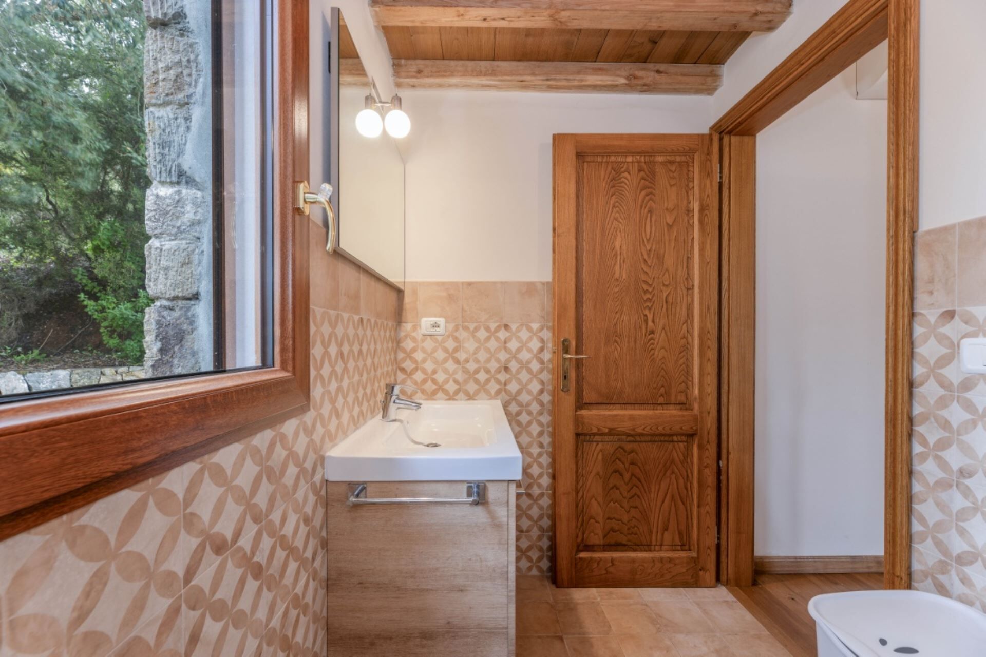 A bathroom with a wooden ceiling, a sink, a mirror, and a door.