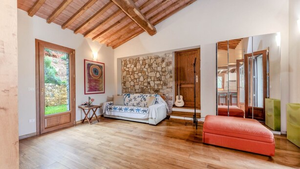 Ein geräumiger Raum mit Holzboden, einer Steinwand, einem Sofa, einem roten Hocker und einer Gitarre.