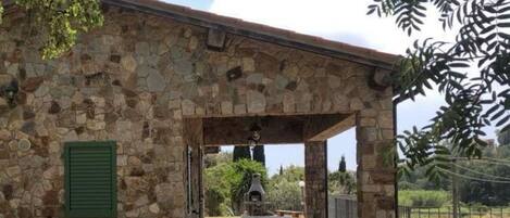 A stone building with a covered outdoor area featuring a stone bench and a grill.