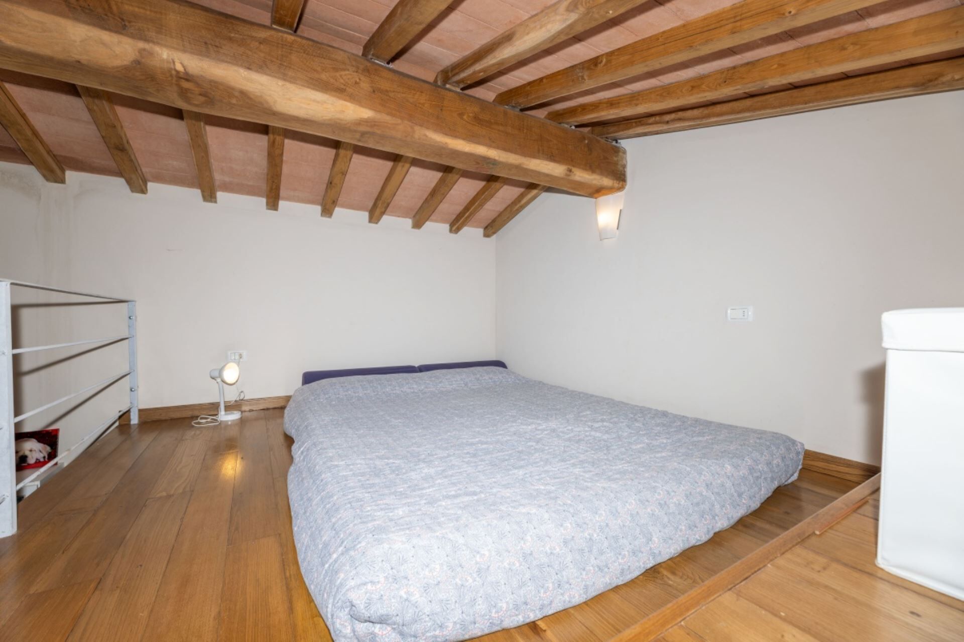 A small, sparsely furnished room with a wooden ceiling, a single bed, a small desk, and a white radiator.