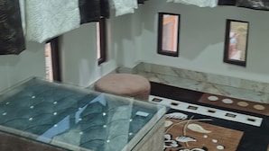 A room with a glass-top table, a brown sofa, patterned curtains, and a decorative rug. - Crown Pavilion Resort  (Fatehabad)