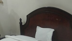 A bed with a wooden headboard, white bedding, and a nightstand beside it. - Crown Pavilion Resort  (Fatehabad)
