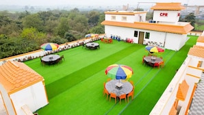 A rooftop terrace with multiple tables and chairs, a CPR building, and a green lawn. - Crown Pavilion Resort  (Fatehabad)