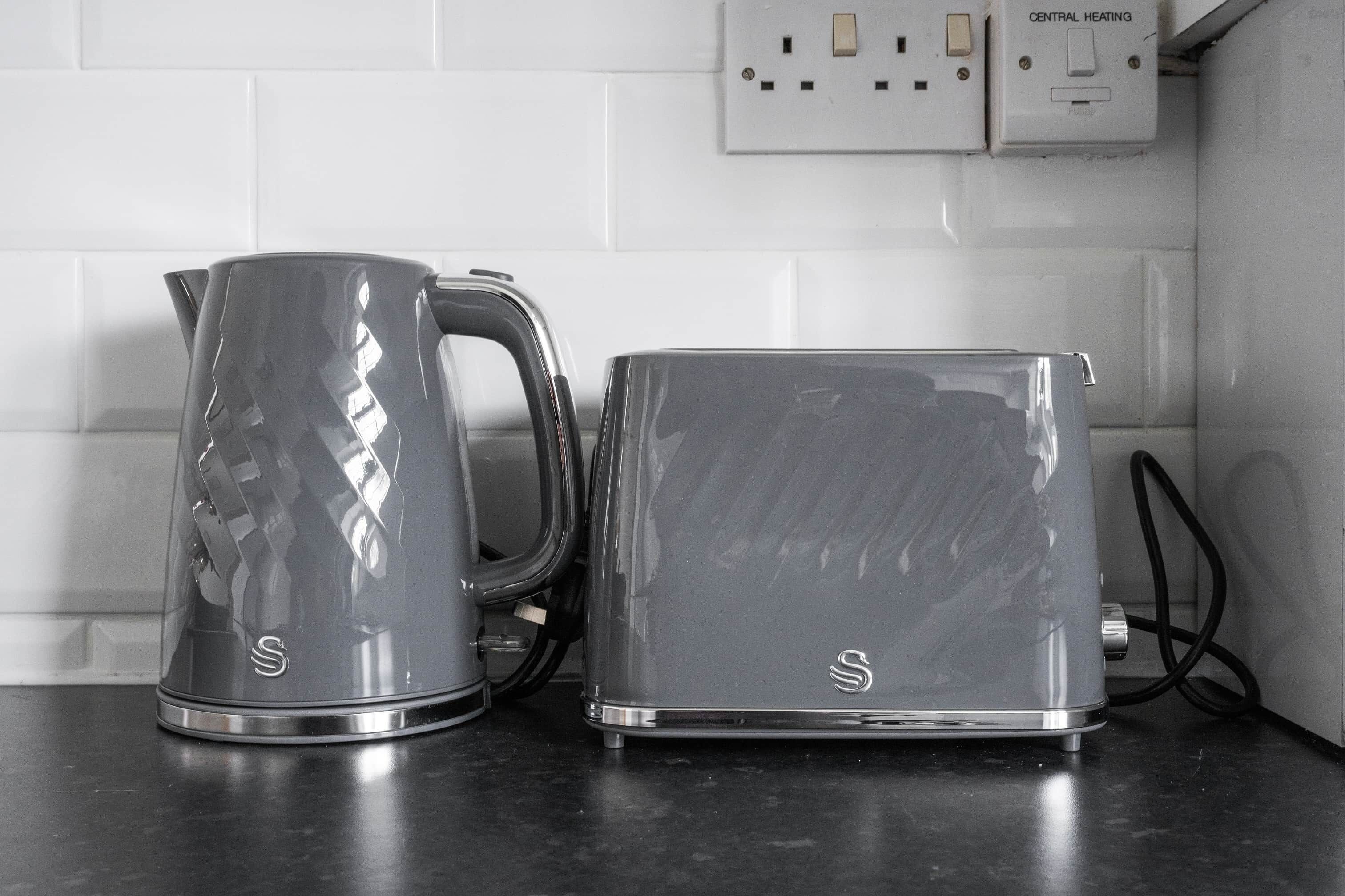 Een keuken met een waterkoker en broodrooster op het aanrecht, een stopcontact en een schakelaar met de tekst 'CENTRAL HEATING'.