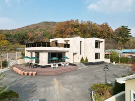 A modern building with a flat roof, large windows, and a paved courtyard with outdoor seating.