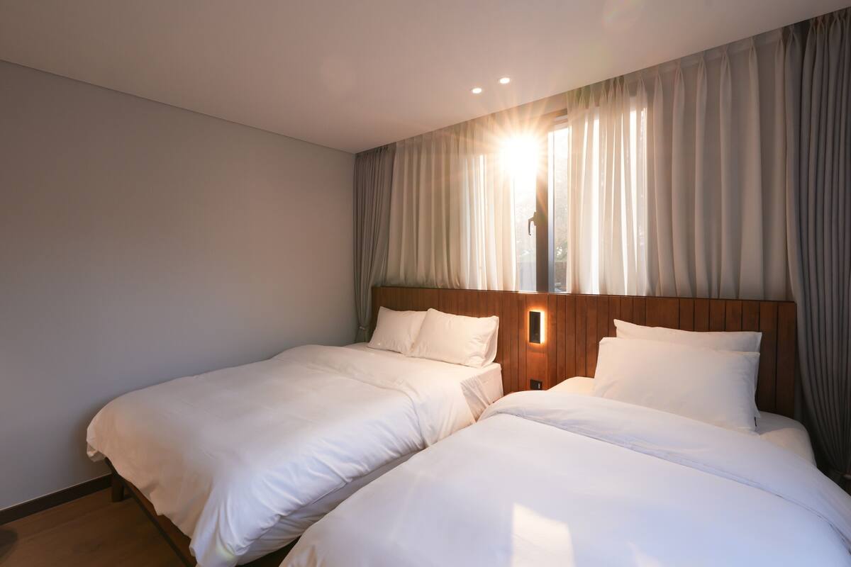 A hotel room with two beds, wooden headboards, and a large window with curtains.