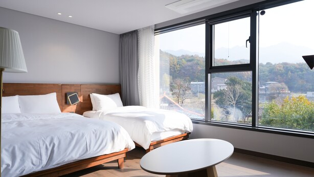 A modern hotel room with two beds, a bedside table, and a large window offering a view of the city and mountains. - laforet space (Gongju)