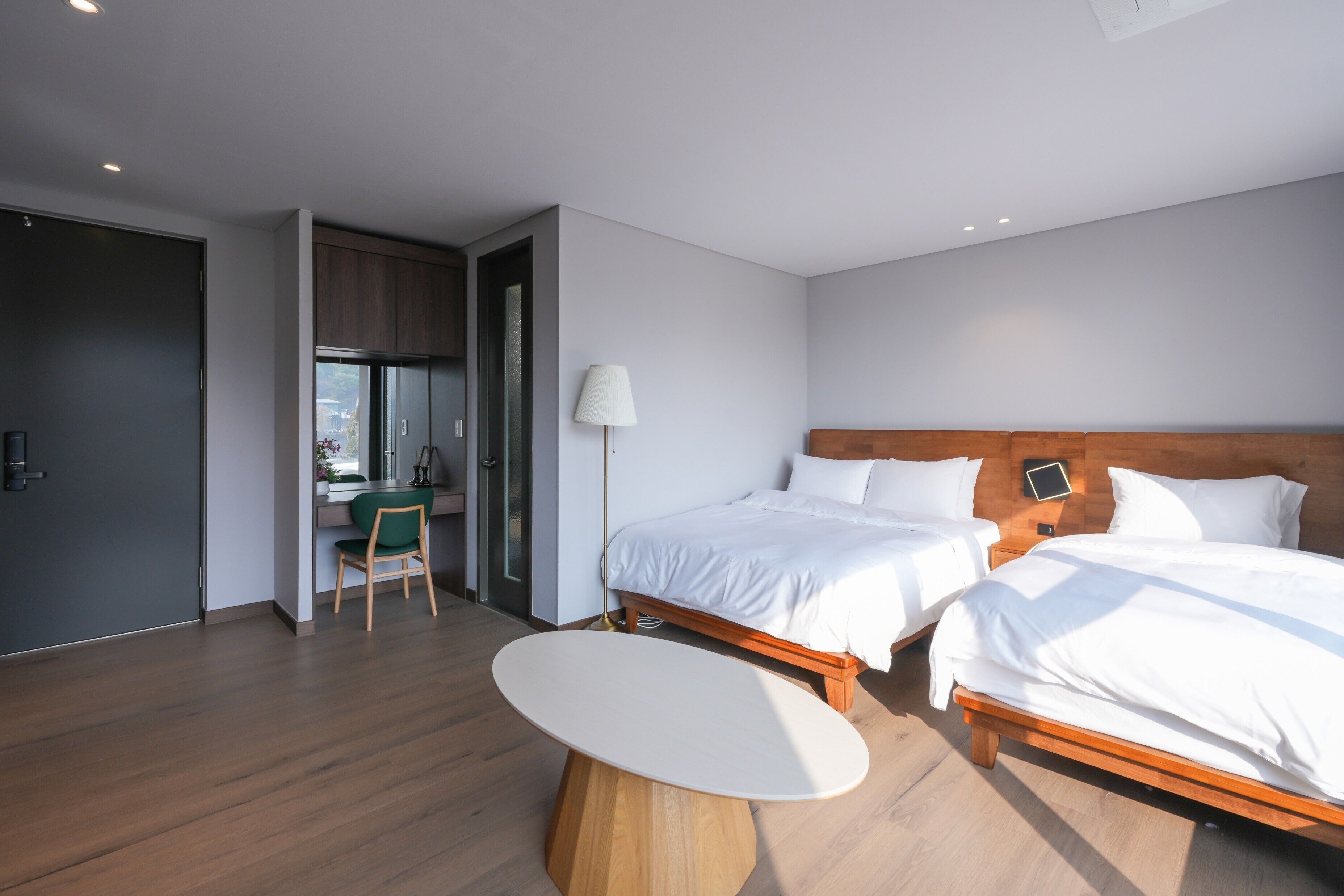 A modern hotel room with two beds, a desk, and a chair.