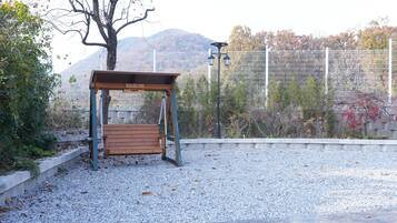 Un banco de madera bajo un refugio, con suelo de grava, rodeado de una cerca y árboles.