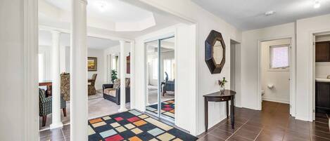 A spacious hallway with white walls, a patterned rug, and a large mirror.