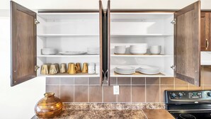 A kitchen with open wooden cabinets containing white plates, bowls, and golden mugs. - 4 Tvs, King Bed, Across Recreational Park, Tennis Court, Near Commercial Center (Ajax)