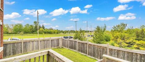 A wooden deck with a grassy area, a brick building, and a clear blue sky with clouds.