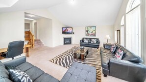 A spacious living room with a high ceiling, a fireplace, a television, and a large window. - 4 Tvs, King Bed, Across Recreational Park, Tennis Court, Near Commercial Center (Ajax)
