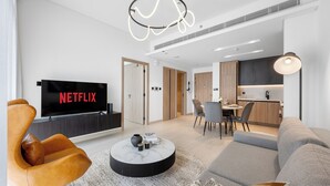 A modern living room with a flat-screen TV, leather armchair, round coffee table, and a grey sofa. - Modern Apartment with Rooftop Amenities (Dubai)