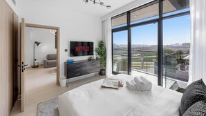A modern hotel room with a large bed, a flat-screen TV, and a view of the cityscape through large windows. - Modern Apartment with Rooftop Amenities (Dubai)