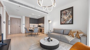 A modern living room with a grey sofa, a round coffee table, and a dining area with a table and chairs. - Modern Apartment with Rooftop Amenities (Dubai)