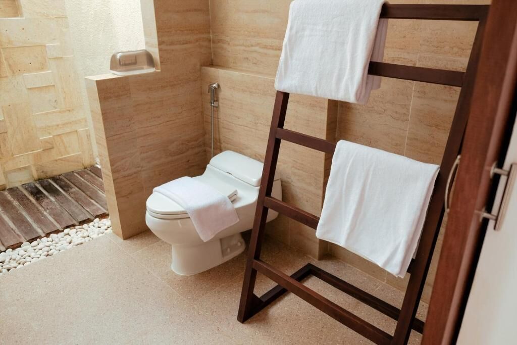 A bathroom with a toilet, a wooden towel rack, and a shower area.