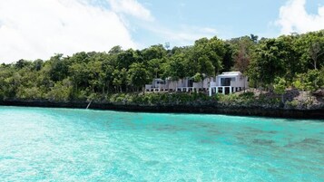 A coastal property with a modern building surrounded by lush greenery and turquoise waters.