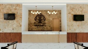 A reception area with a stone wall, a wooden reception desk, and two televisions mounted above it. - Arasatu Villas and Sanctuary (Maratua Island)