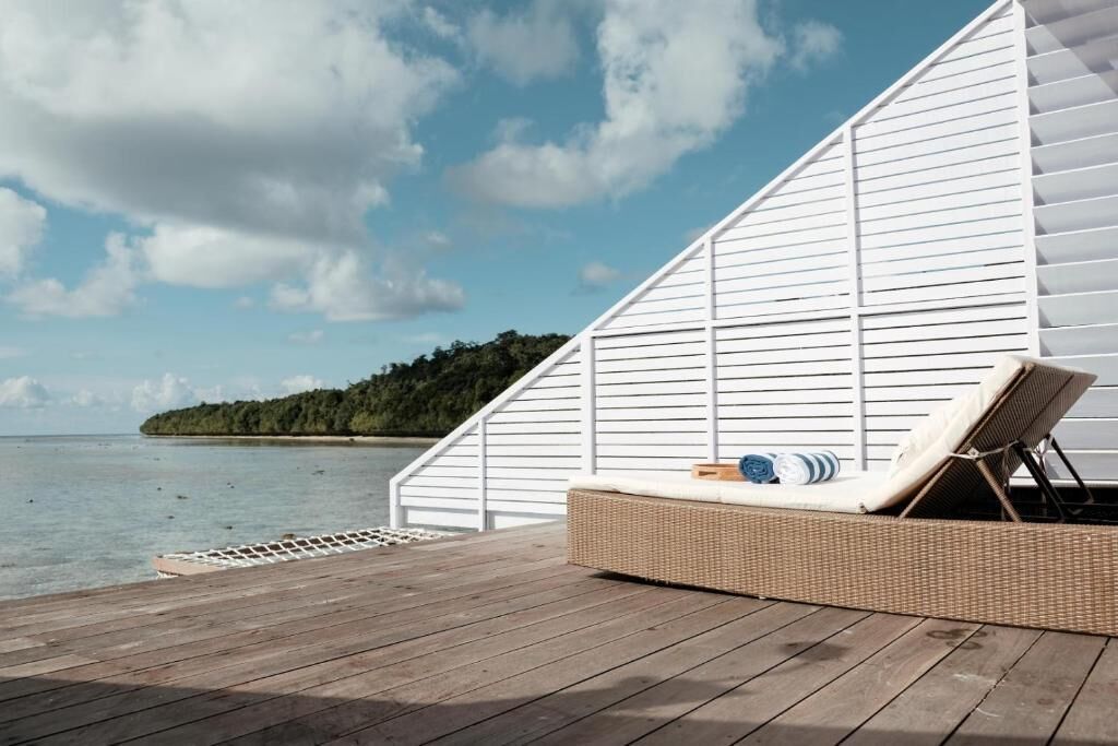 A wooden deck with a white wall and a wicker lounge chair.