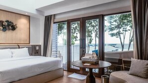 A hotel room with a bed, a sofa, a small table, and a view of the sea through large windows. - Arasatu Villas and Sanctuary (Maratua Island)