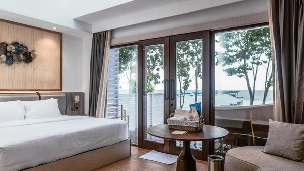 Habitación de hotel con cama, sofá, una mesita y vista al mar a través de amplios ventanales.