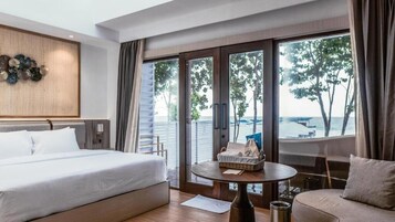 A hotel room with a bed, a sofa, a small table, and a view of the sea through large windows.