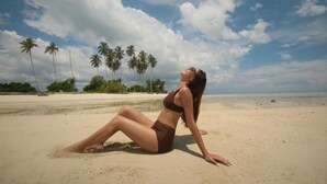 A person sitting on a sandy beach with palm trees in the background. - Arasatu Villas and Sanctuary (Maratua Island)