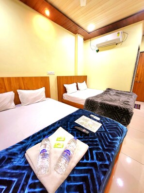 Ein Hotelzimmer mit zwei Betten, einer blauen, gemusterten Tagesdecke, einer Fernbedienung und einer Wasserflasche auf dem Bett.