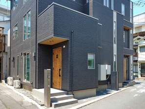Un edificio moderno con fachada oscura, una puerta de madera y una ventana pequeña.