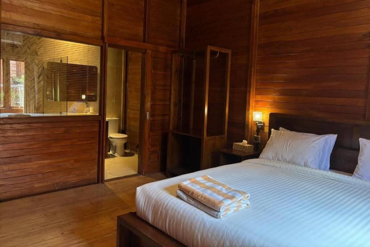 Una habitación con piso de madera, una cama, una mesita de noche y una ventana con persianas.
