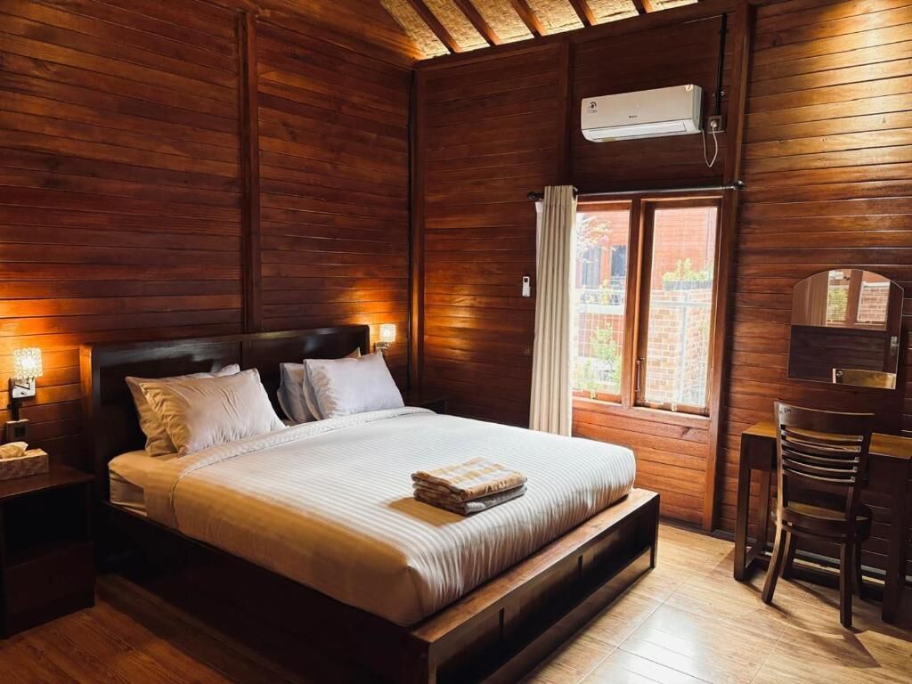 A wooden-paneled bedroom with a bed, bedside tables, a desk, and a chair.