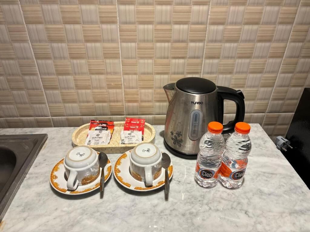 Una encimera de cocina con una cafetera, dos tazas, una bandeja con sobres de café y dos botellas de agua.