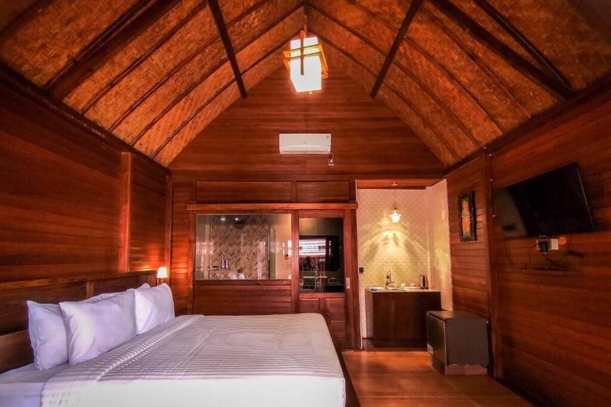 Dormitorio de cabaña de madera con cama, un escritorio pequeño, un televisor y un baño con ducha.