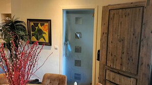 Een kamer met een blauwe deur, een houten deur, een lijst met een schilderij en een plant.